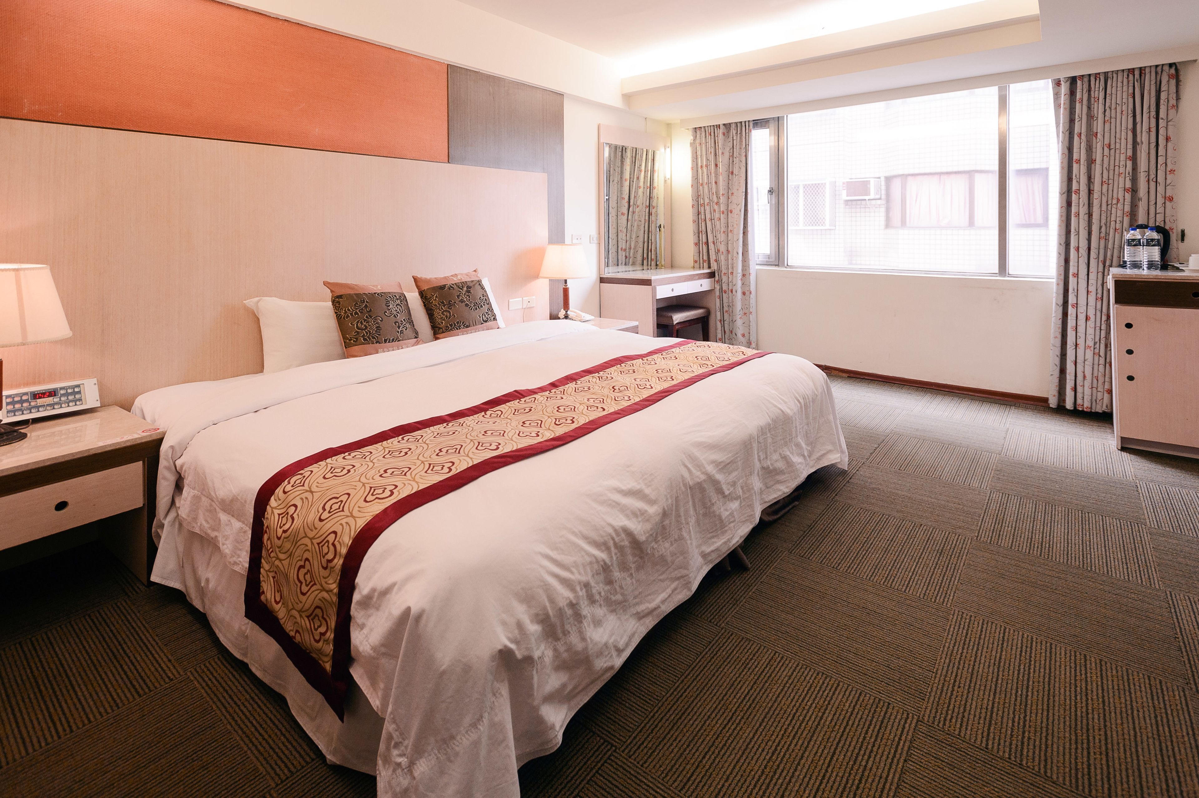 A hotel room with a large bed, a desk, a chair, a wardrobe, and a window with curtains.
