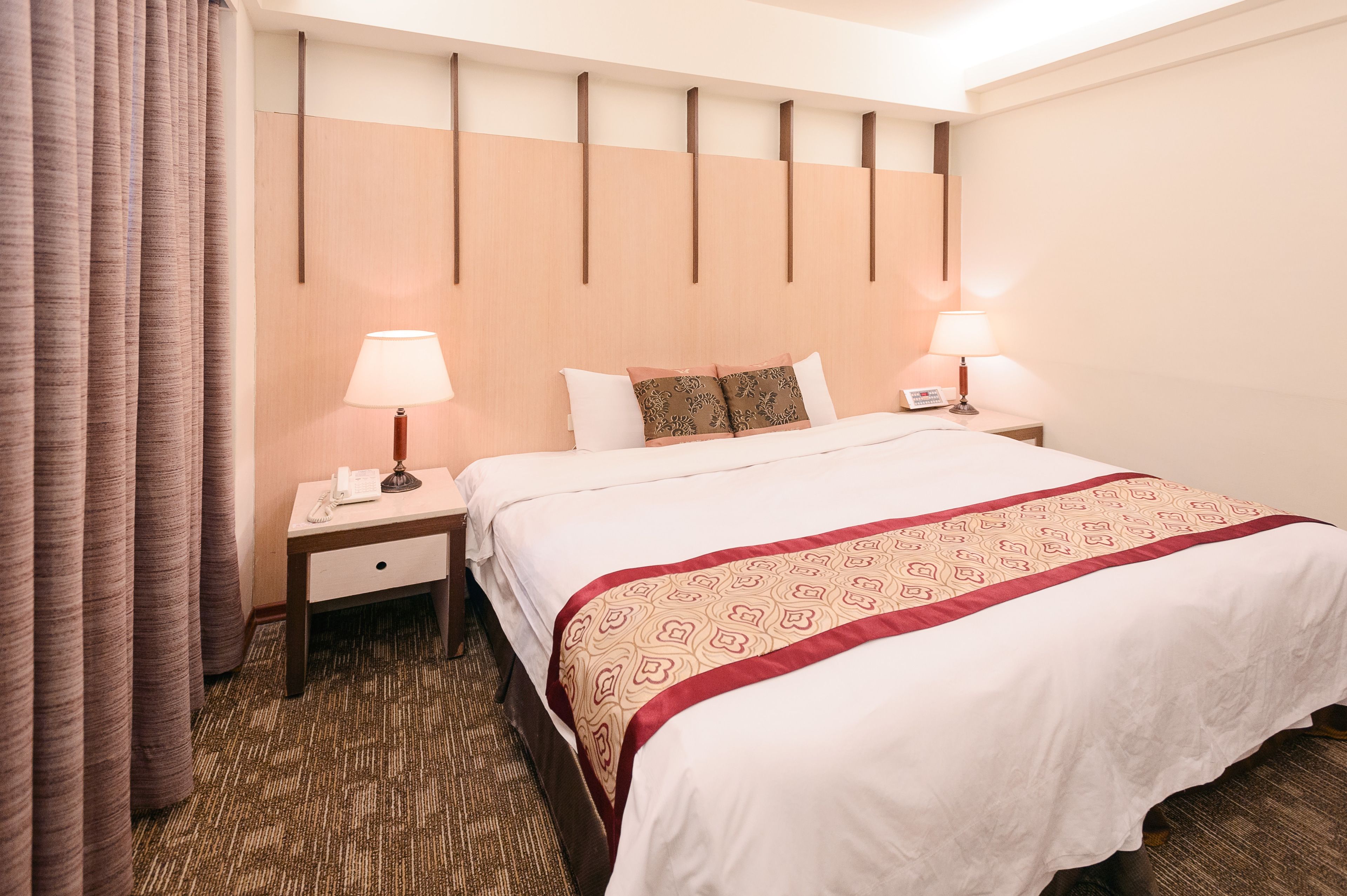 Una habitación de hotel con una cama grande, dos mesitas de noche con lámparas, un teléfono y suelo cubierto de alfombra.