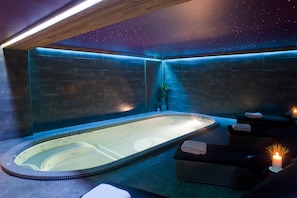 Relax in a serene spa area with a large hot tub, dark walls, and a starry night sky ceiling.