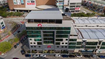 Un hotel de varios pisos con un llamativo logotipo de Rocana, rodeado de edificios comerciales y zonas de estacionamiento.