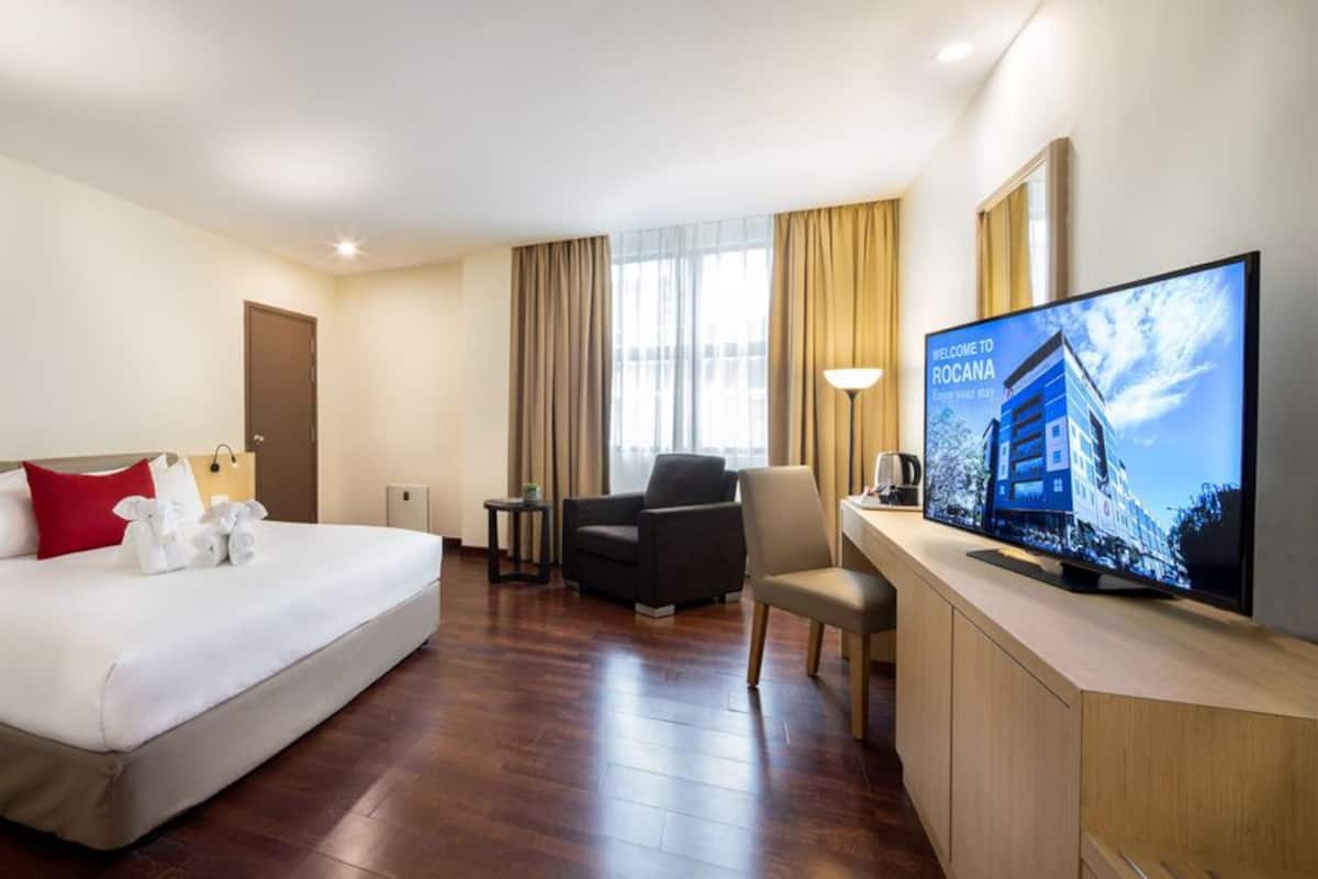 A hotel room with a bed, a desk, a chair, a television, and a window with curtains.