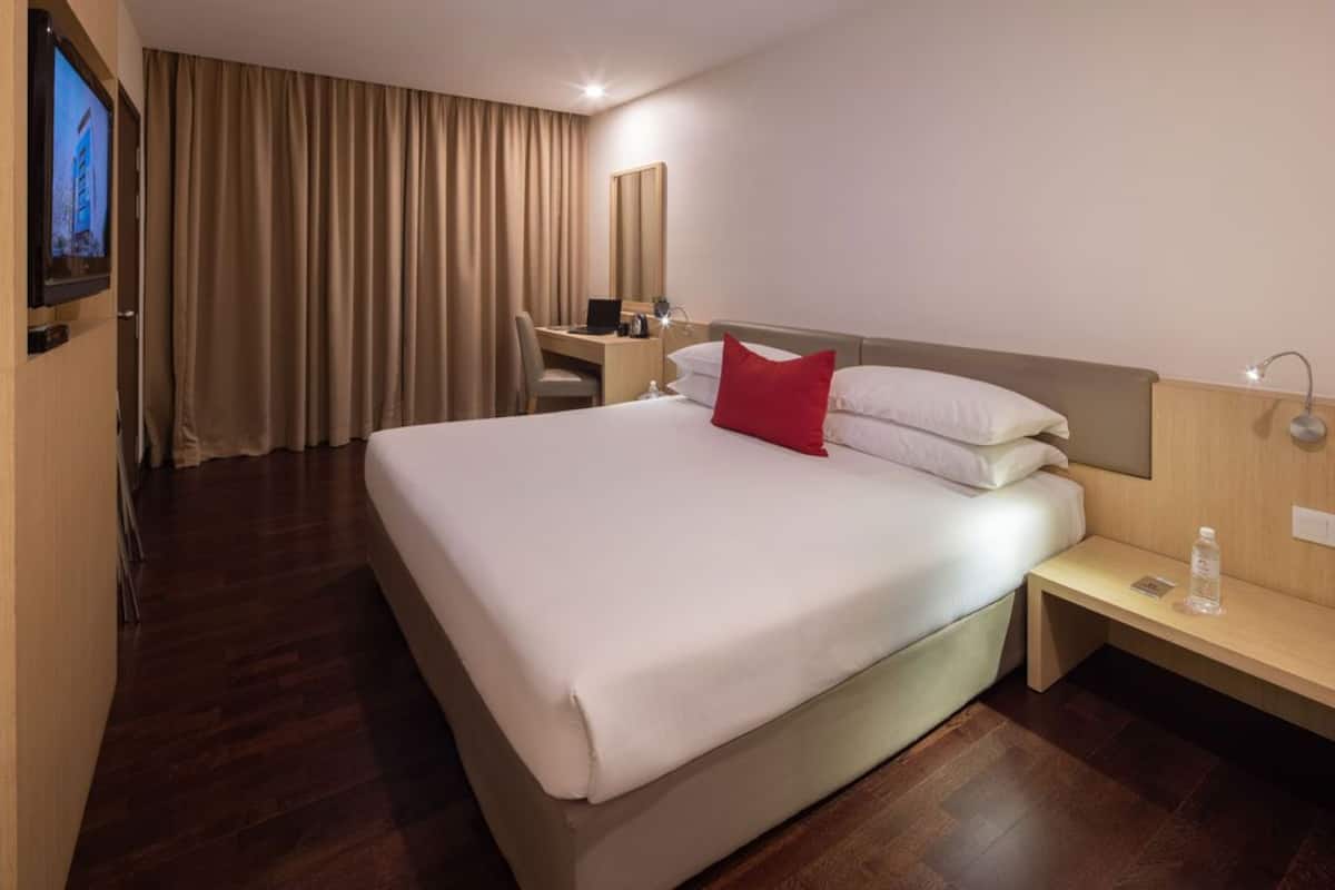 A hotel room with a large bed, a desk with a chair, a television, and a window with curtains.