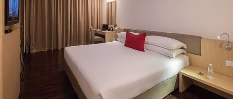 Camera d'albergo con un letto grande, una scrivania con una sedia, una televisione e una finestra con tende.