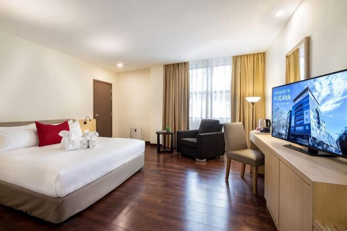 A hotel room with a bed, a desk with a television, a chair, and a window with curtains.