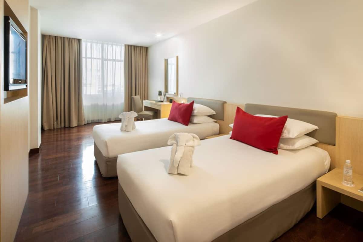 A hotel room with two beds, a desk, a chair, a TV, and a window with curtains.