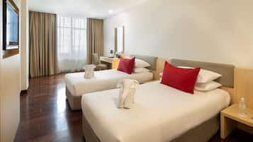 A hotel room with two beds, a desk, a chair, a TV, and a window with curtains.