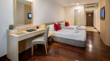 Una habitación de hotel con un escritorio de madera, dos camas, una silla, un televisor y un espejo.