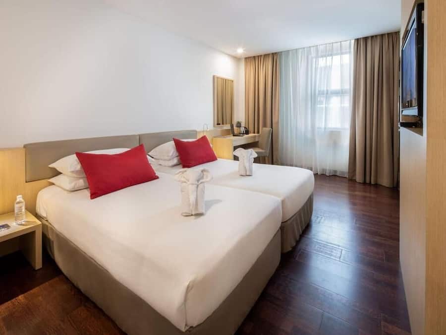 A hotel room with two beds, a desk, a chair, a TV, and a large window with curtains.