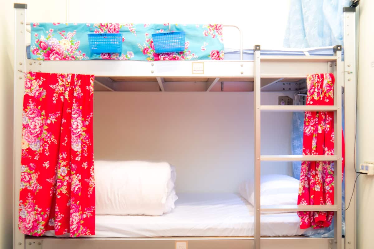 A bunk bed with floral curtains, a small shelf, and a ladder.