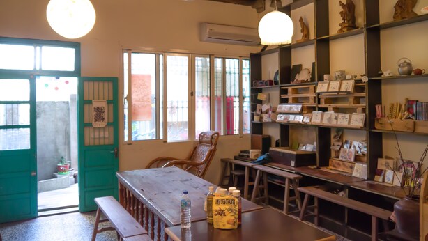 A cozy cafe with wooden furniture, a green door, and shelves with various items. - Smalleye Backpacker (Lukang)