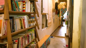 A narrow hallway with wooden bookshelves filled with books, a bench, and a door leading to another room. - Smalleye Backpacker (Lukang)