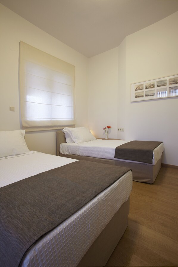 A hotel room with two beds, a large window with blinds, a framed picture on the wall, and a wooden floor.