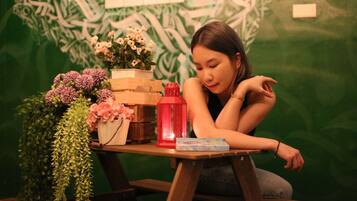 A person sitting at a wooden table with a red lantern, a book, and various flowers.