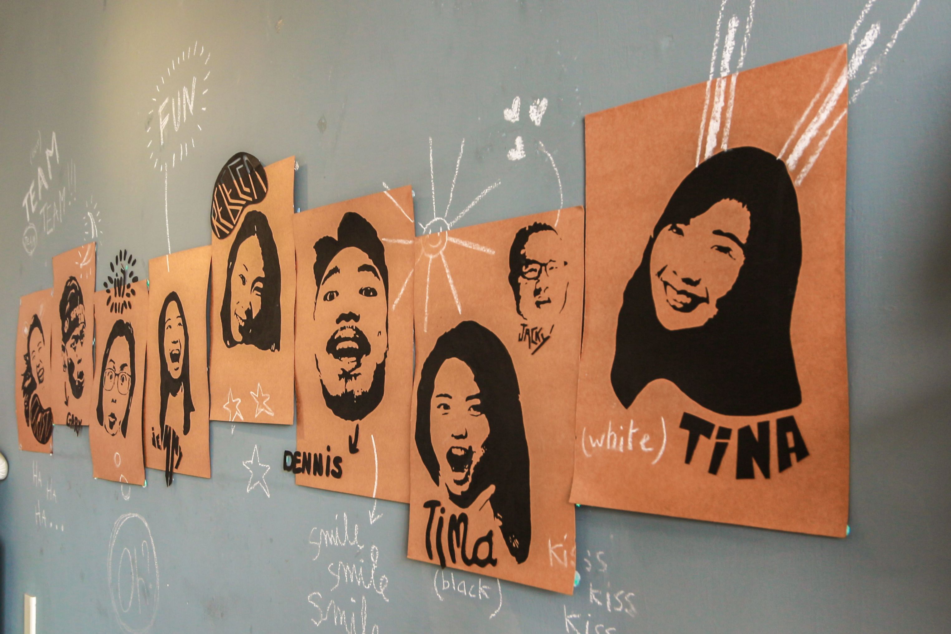 A wall with multiple brown paper bags, each with a person's name and a drawing of their face.