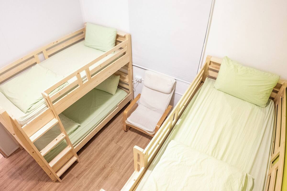 A room with two bunk beds, a small chair, and a white wall.