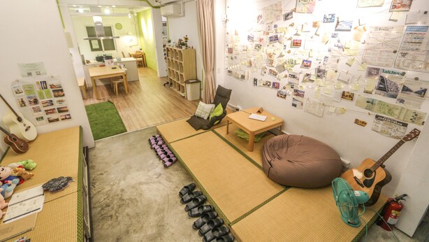Una habitación con esteras de tatami, una guitarra, un ventilador y una pared llena de fotos.