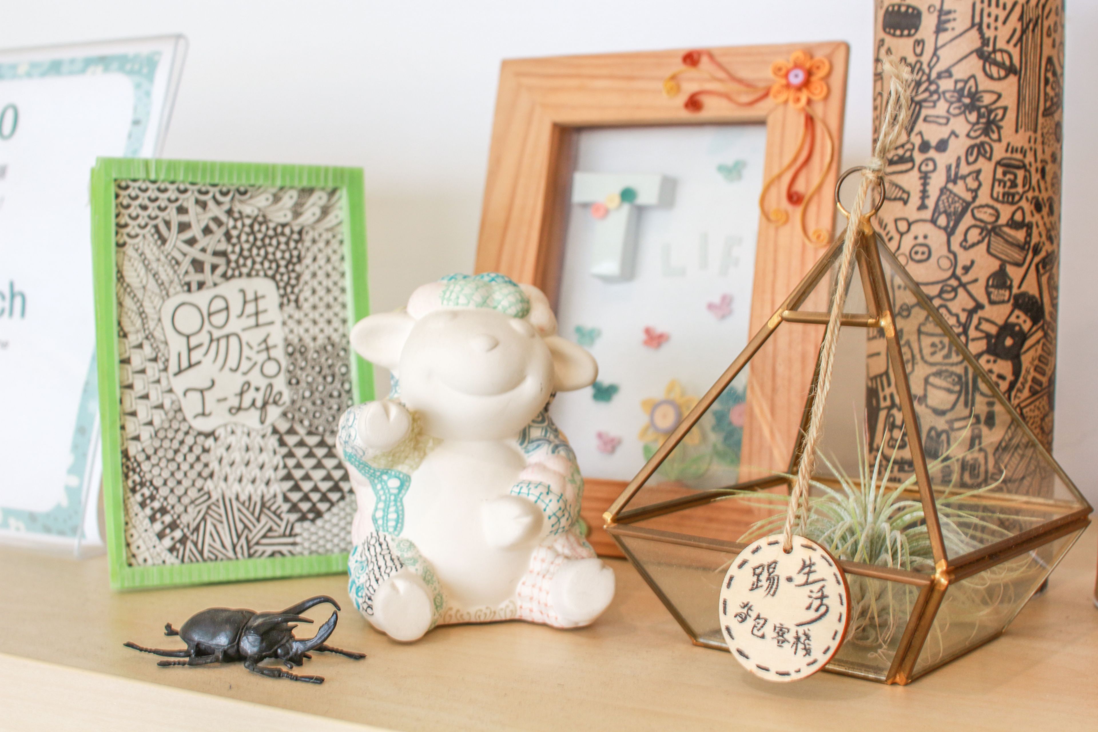 A shelf with decorative items including a ceramic sheep, a framed picture, a glass terrarium, and a beetle.