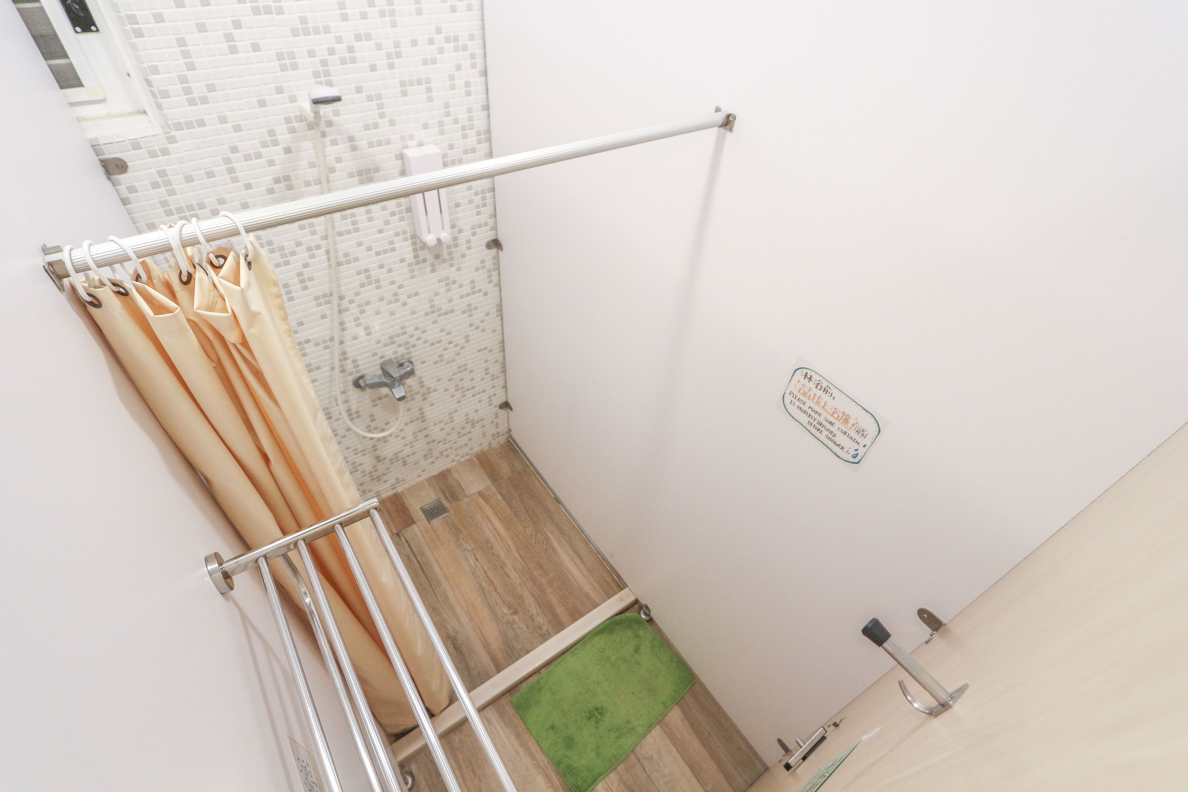 Ein Badezimmer mit Dusche, Handtuchhalter, einer grünen Matte und einem Schild an der Wand.