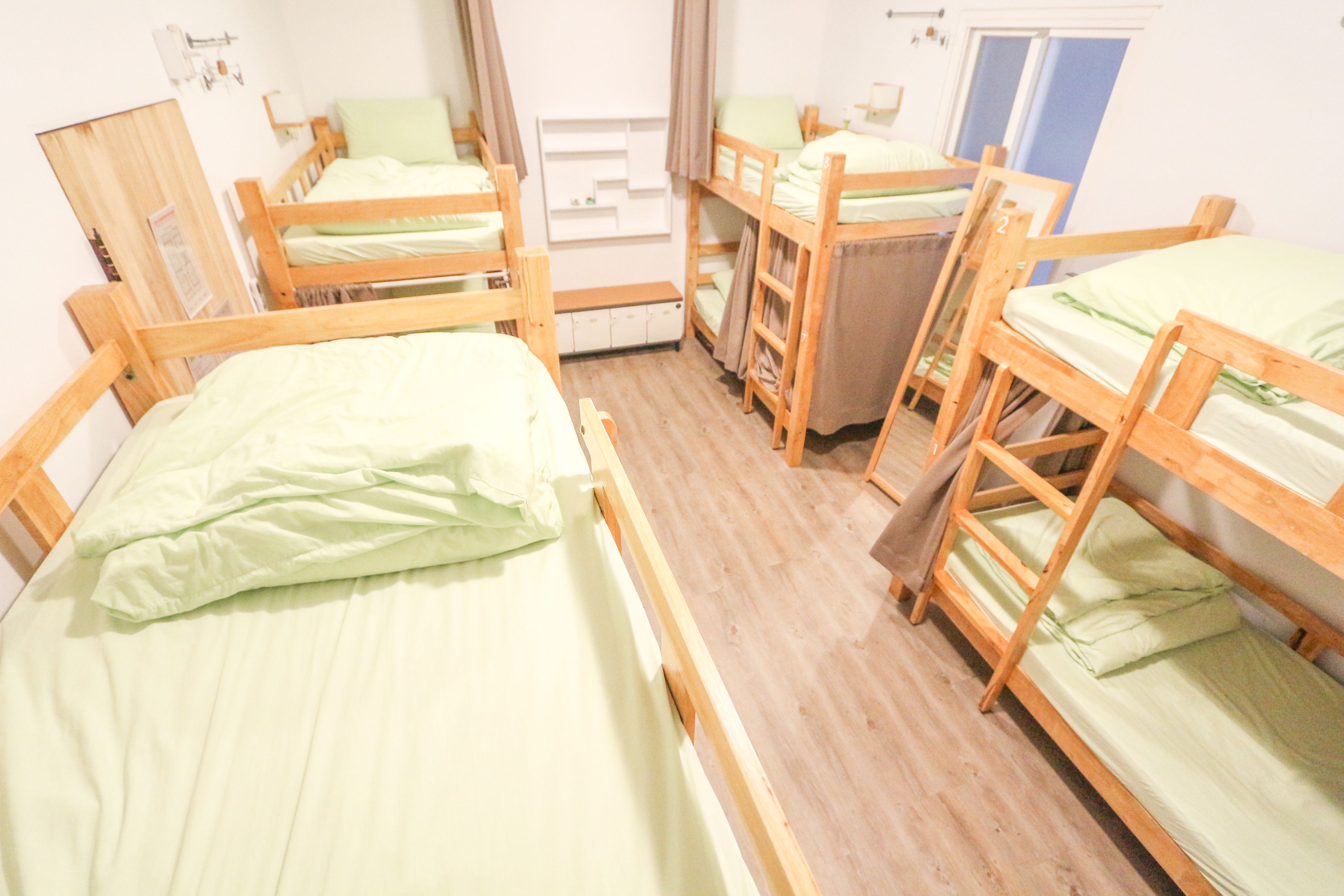 A dormitory room with bunk beds, wooden floors, and a window.