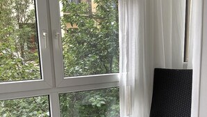 A room with a large window, a wicker chair, a small ottoman, and a radiator. - Pensión Donostiarra (San Sebastián)