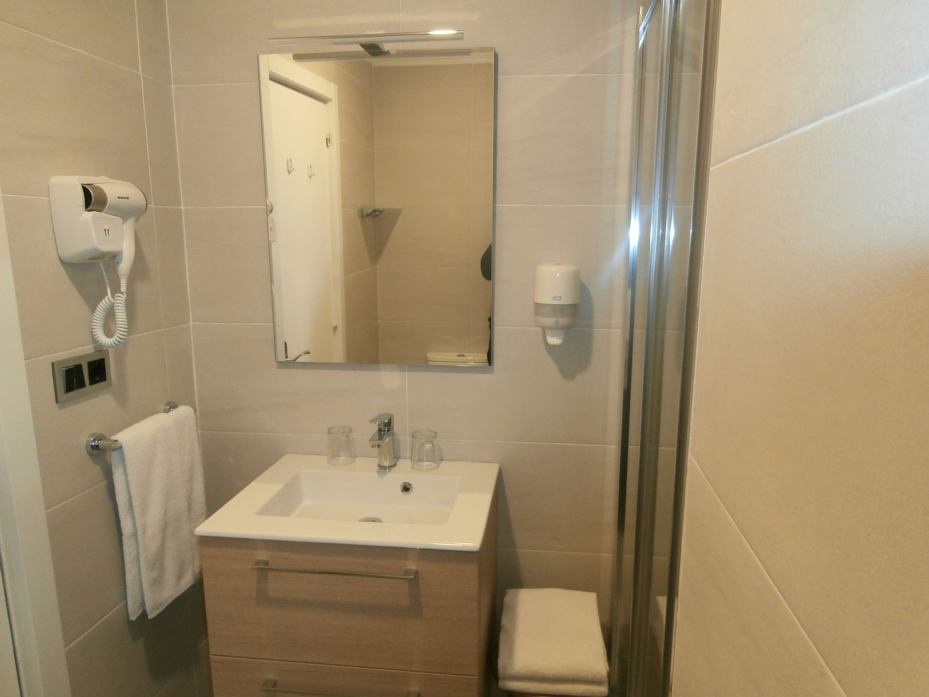 Een badkamer met een wastafel, spiegel, handdoekhouder en een losse haardroger.