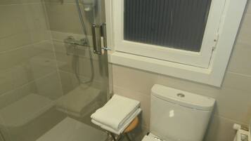 Une salle de bain avec une douche à parois de verre, des toilettes et une fenêtre située au-dessus des toilettes.