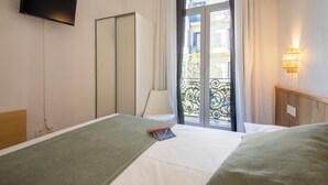 A hotel room with a bed, a TV mounted on the wall, a window with curtains, and a balcony with a railing. - Pensión Donostiarra (San Sebastián)