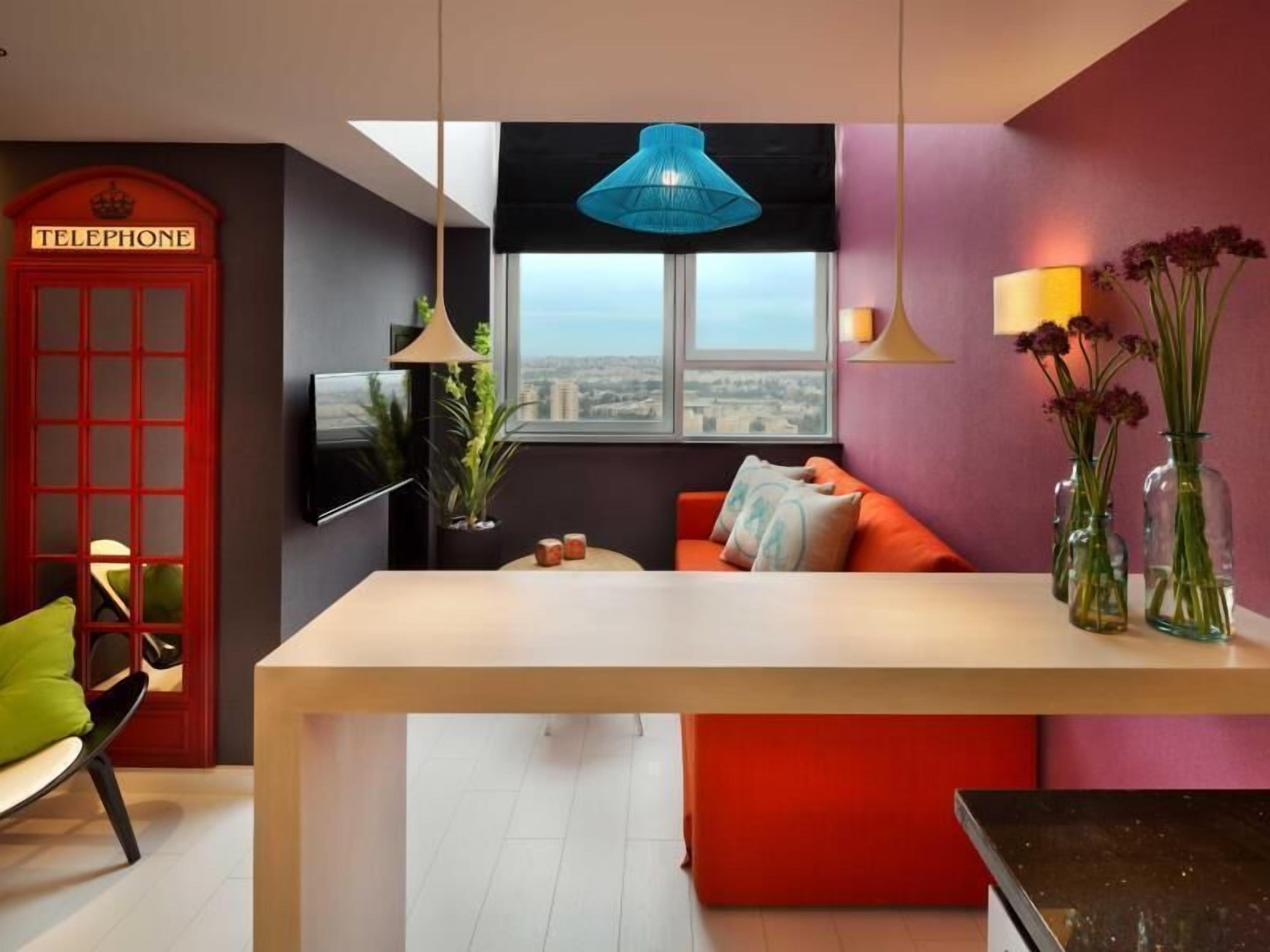 Un interior moderno con una cabina telefónica roja, un sofá, una mesa y vistas por una ventana.