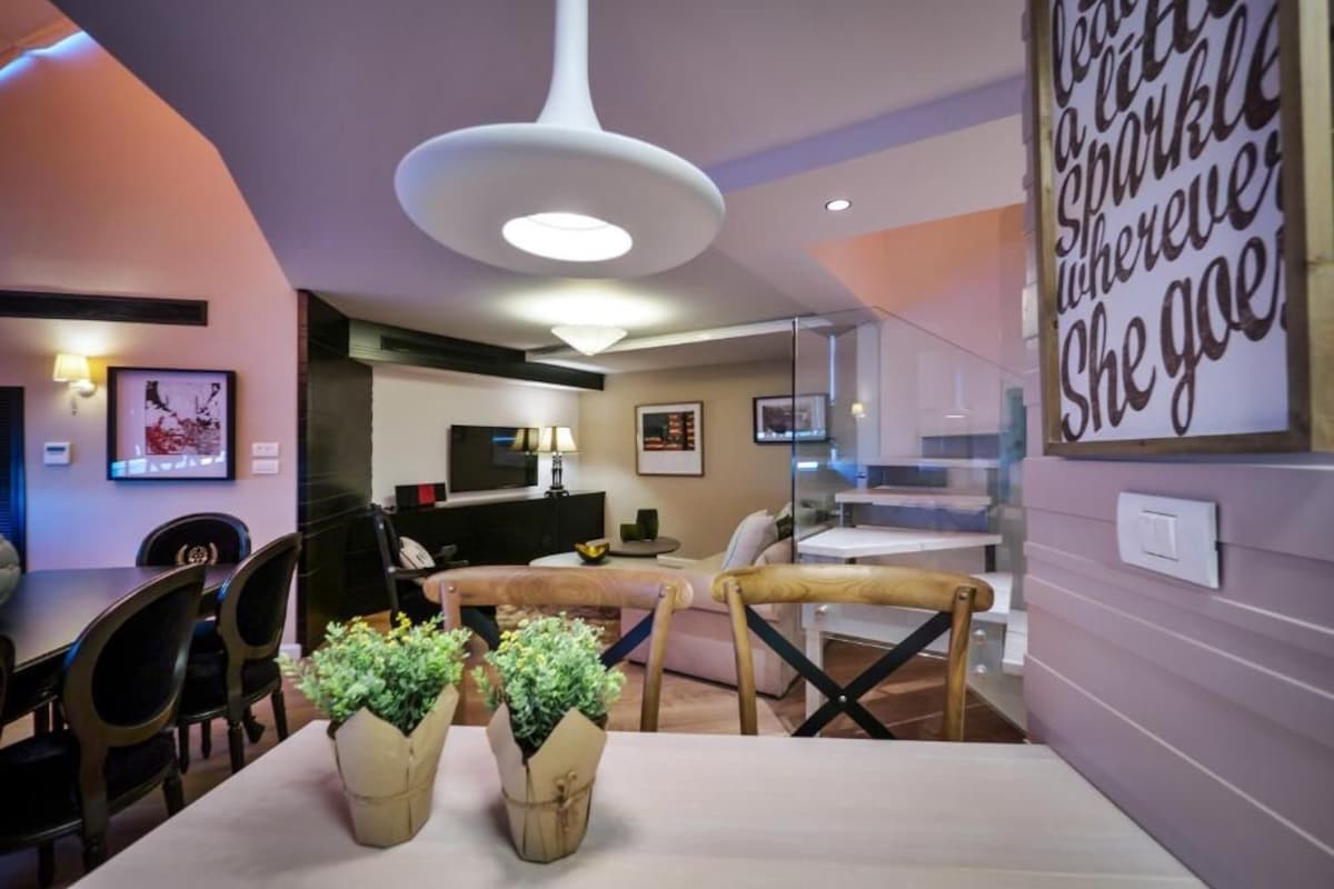 A modern living room with a dining area, a TV, and a staircase.