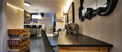 A modern dining area with a wooden table and bench, a staircase leading to a kitchen, and a wall-mounted mirror.