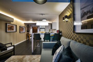A modern living room with a sofa, a coffee table, and a dining area with chairs and a kitchen in the background.