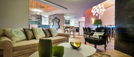 A modern living room with a sofa, a coffee table, and a dining area with chairs and a chandelier.