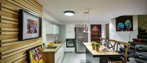A modern kitchen with wooden paneling, a central island, stainless steel appliances, and a dining area with a black leather chair.