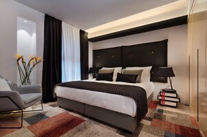 Habitación de hotel moderna con una cama grande, una mesita de noche con lámpara, una silla y una planta decorativa.