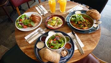 A round wooden table with various dishes, including salads, bread, and a croissant. There are two glasses of orange juice and a plate with a croissant.