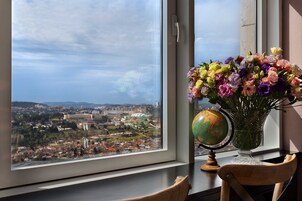 Un escritorio con un globo terráqueo y un florero junto a una ventana que da a vistas de la ciudad.
