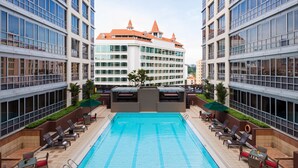 Ein Schwimmbecken mit Liegestühlen und Sonnenschirmen, umgeben von Hochhäusern mit einem markanten orangefarbenen Dach.