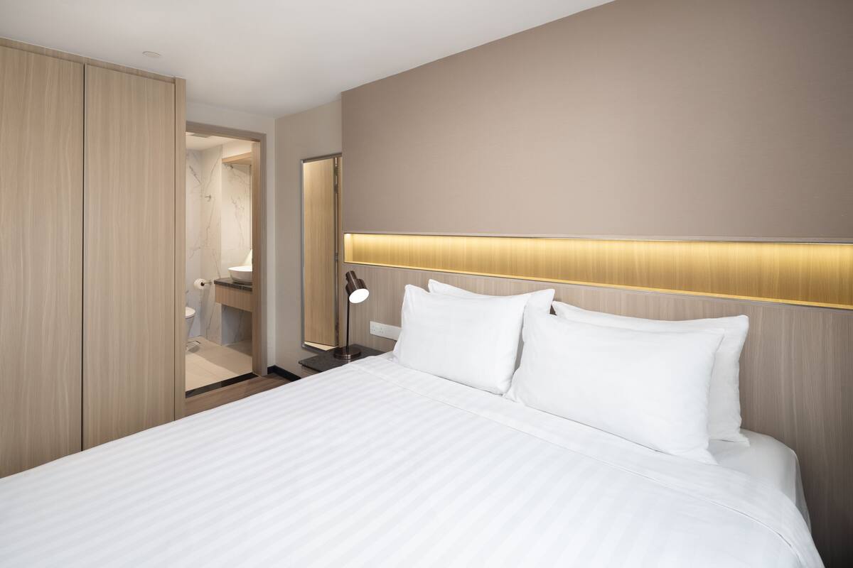 A hotel room with a large bed, a bedside table with a lamp, and a wardrobe.