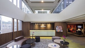 Eine moderne Hotelhalle mit Empfangsschalter, Sitzbereich und großen Fenstern mit Blick auf die Stadt.