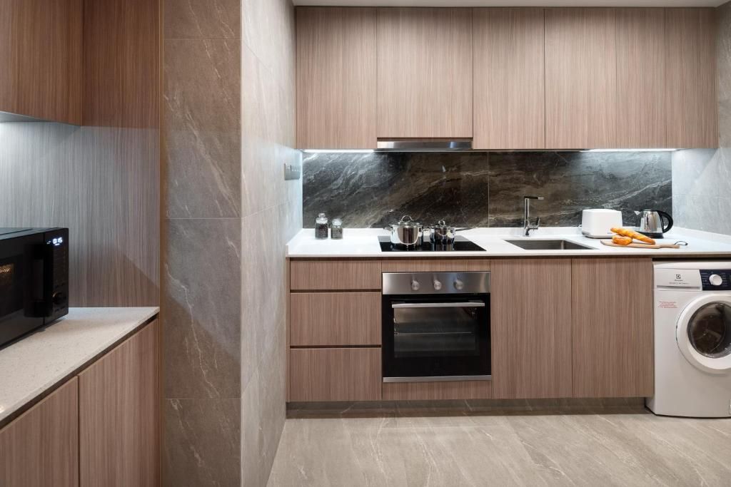 Una cocina moderna con armarios de madera, horno empotrado, microondas, lavaplatos y lavadora.