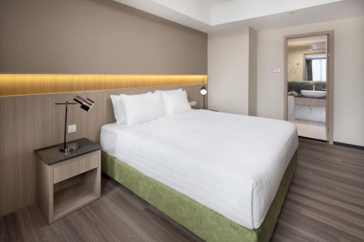 A hotel room with a large bed, a bedside table, a lamp, and a mirror.
