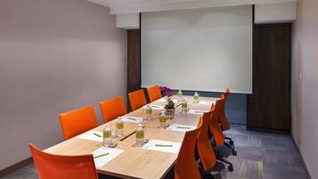 A conference room with a long table, orange chairs, water bottles, and a projector screen.