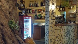 Angolo bar con parete in pietra, frigo Coca-Cola ed scaffali con diverse bottiglie.