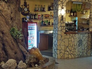 Un área de bar con pared de piedra, un refrigerador de Coca-Cola y estantes con varias botellas.