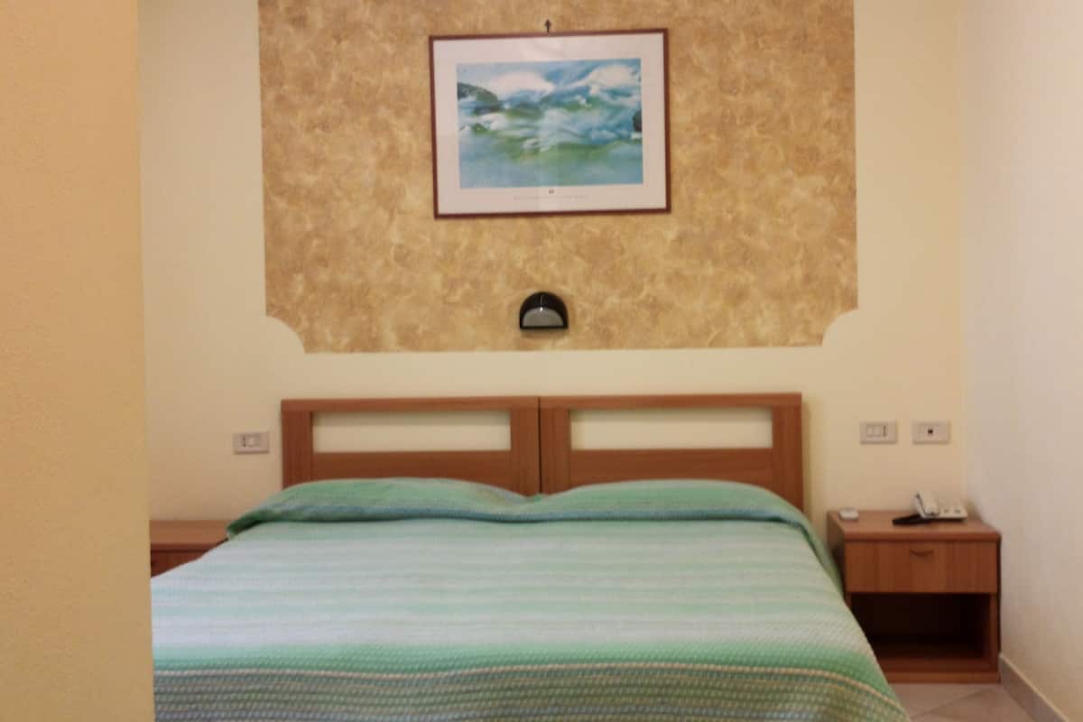 A bedroom with a bed, a nightstand, a wall-mounted lamp, and a framed picture above the bed.