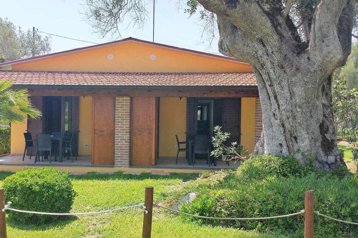 A building with a tiled roof, a brick column, and a covered patio with chairs.