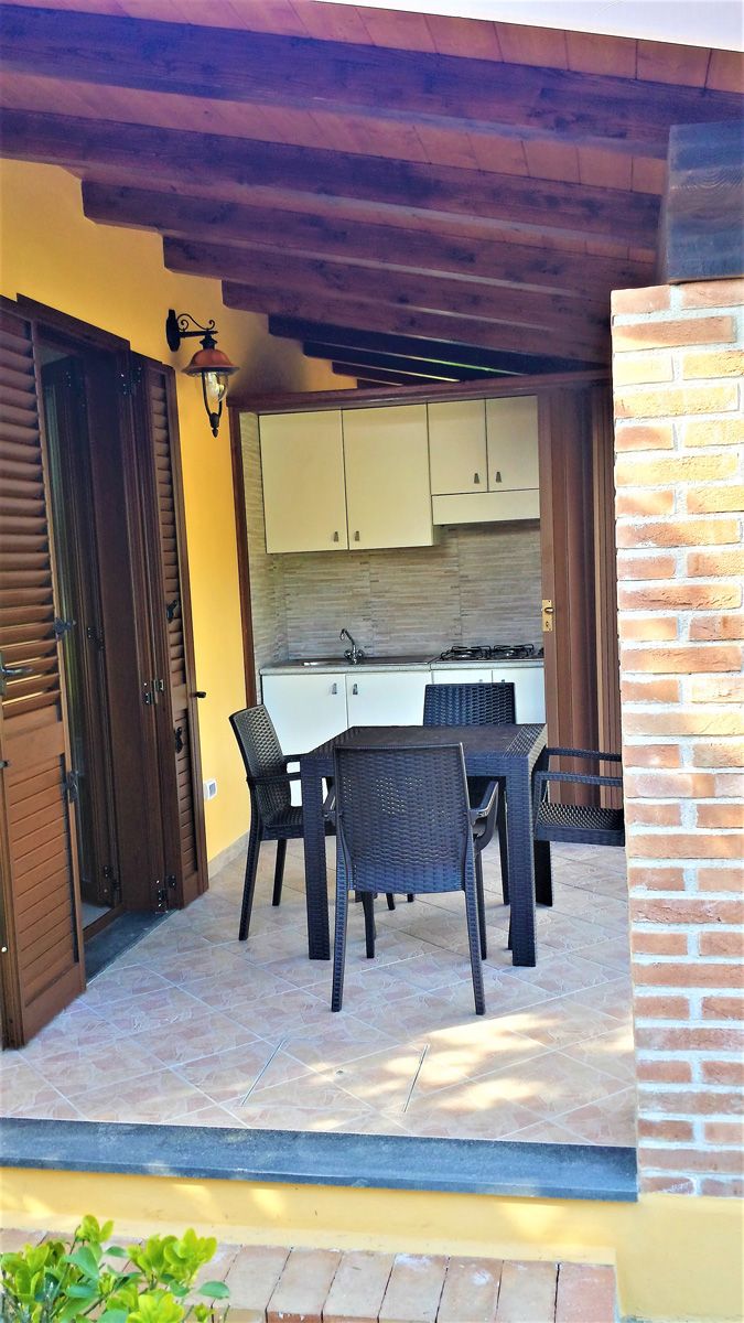 An outdoor patio with a dining table and chairs, a brick wall, and a kitchen area with cabinets and a stove.