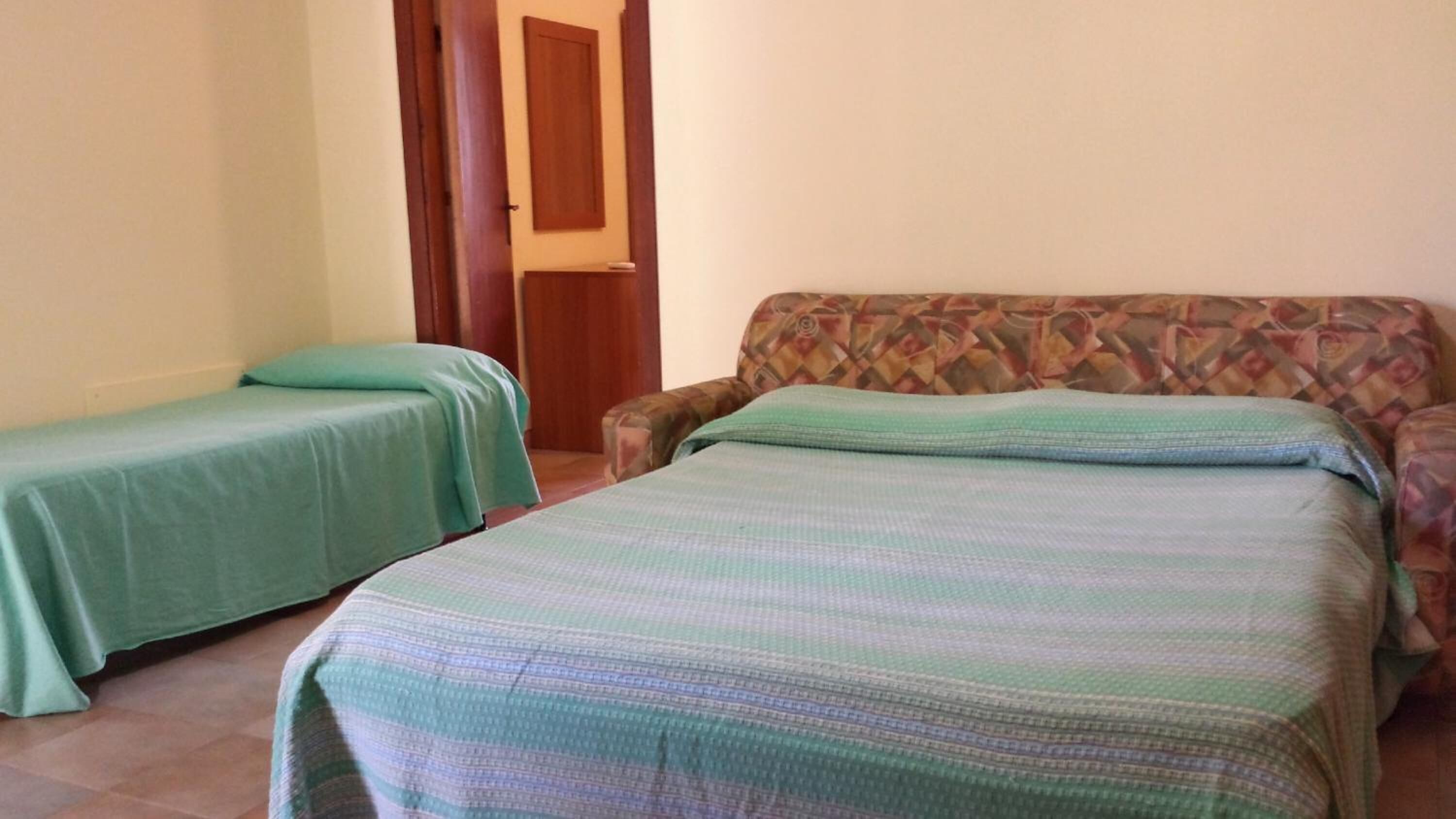 A room with two single beds, a patterned sofa, and a wooden door.
