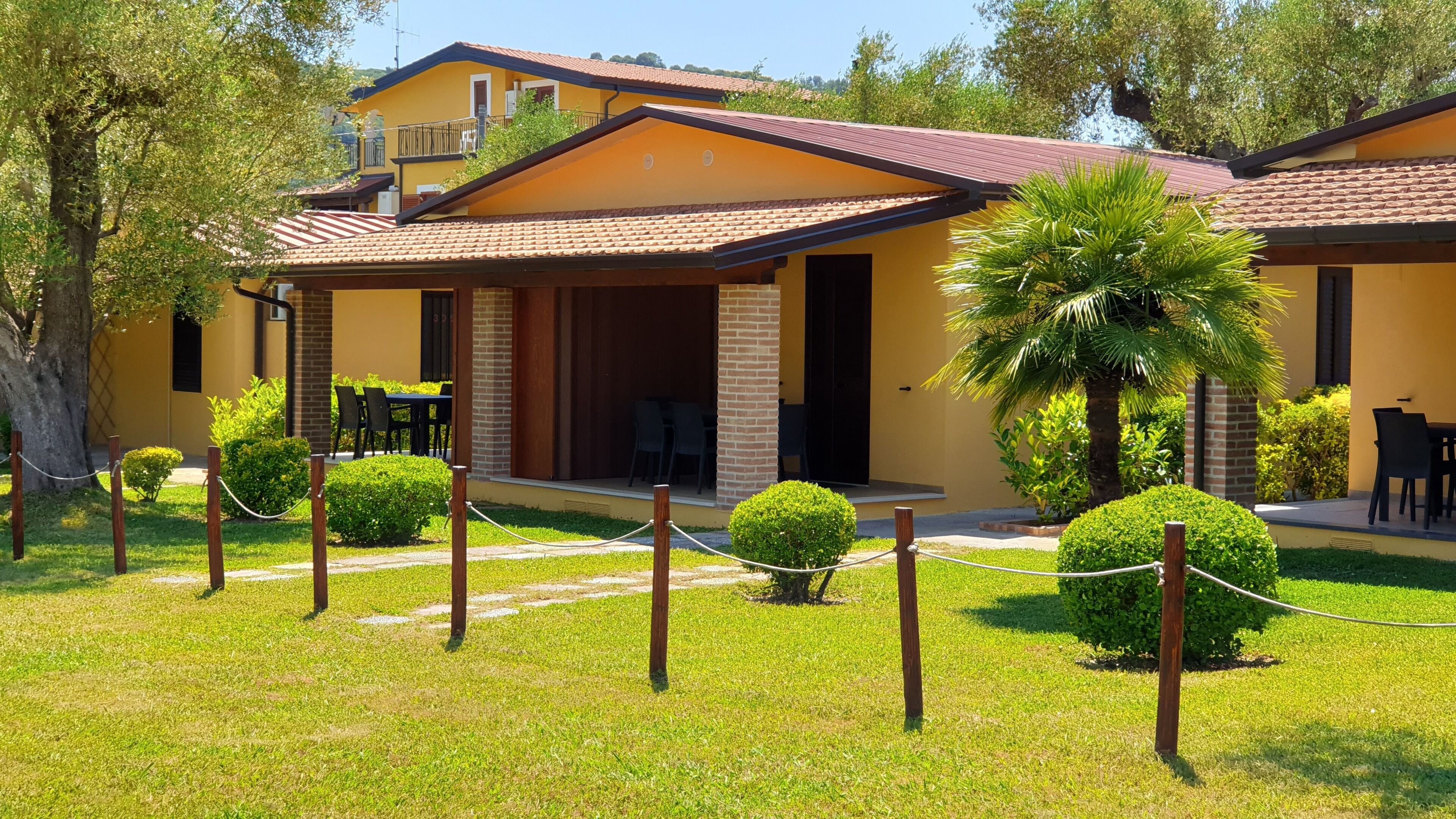 A yellow building with a tiled roof, a covered patio with outdoor seating, and a well-maintained lawn.