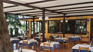 Un ristorante all'aperto con tavoli rivestiti da tovaglie bianche e blu, sedie di legno e piante in vaso.